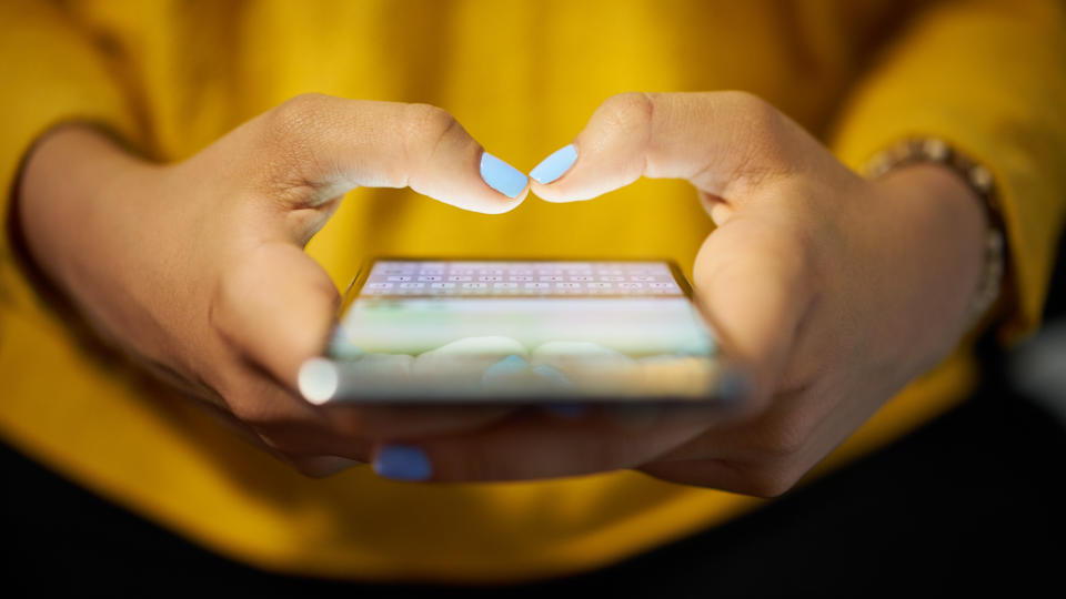 Young woman using cell phone to send text message on social network at night.