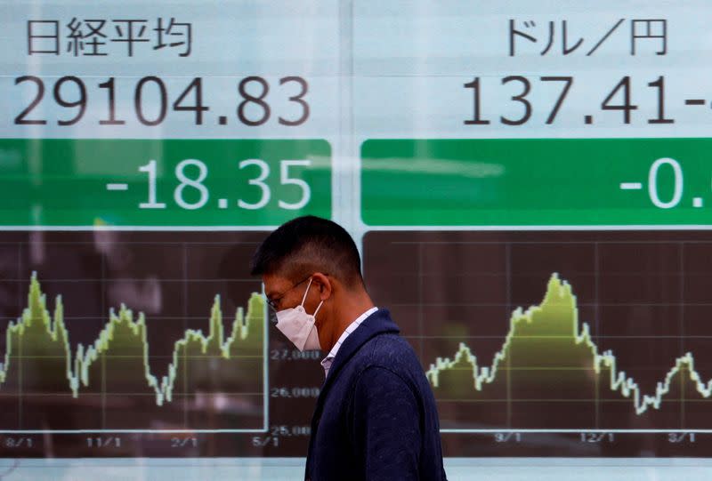 FILE PHOTO: A man walks past an electric monitor displaying Nikkei share average and the Japanese yen exchange rate against the U.S. dollar outside a brokerage in Tokyo