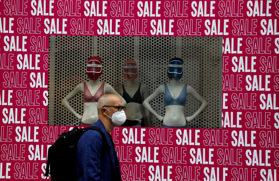 A man wearing a protective face mask walks past a shop window in London, Tuesday, July 14, 2020. Britain's government is demanding people wear face coverings in shops as it has sought to clarify its message after weeks of prevarication amid the COVID-19 pandemic. (AP Photo/Frank Augstein)