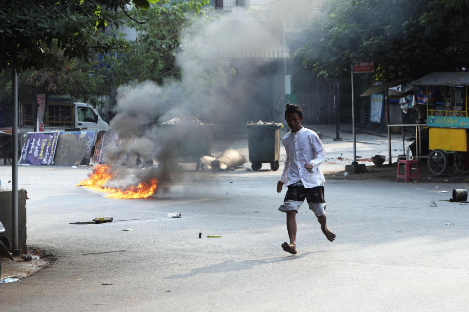 A man crosses the street while fire is seen in front of a road barricade that prevents security forces from advancing in Mandalay, Myanmar Sunday, March 14, 2021. At least four people were shot dead during protests in Myanmar on Sunday, as security forces continued their violent crackdown against dissent following last month's military coup. (AP Photo)