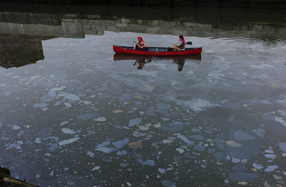 people in a canoe in the canal, which has many chemical and oil spots