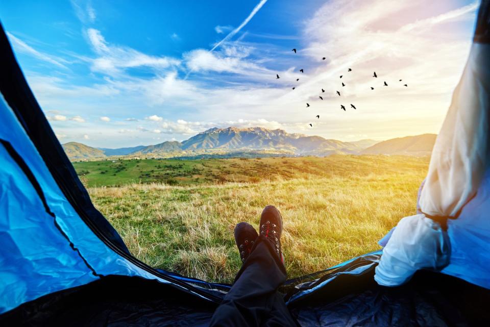 person overlooking nature with feet hanging out of tent while camping