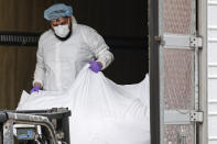 A body wrapped in plastic is loaded onto a refrigerated container truck used as a temporary morgue by medical workers wearing personal protective equipment due to COVID-19 concerns, Tuesday, March 31, 2020, at Brooklyn Hospital Center in the Brooklyn borough of New York. The new coronavirus causes mild or moderate symptoms for most people, but for some, especially older adults and people with existing health problems, it can cause more severe illness or death. (AP Photo/John Minchillo)