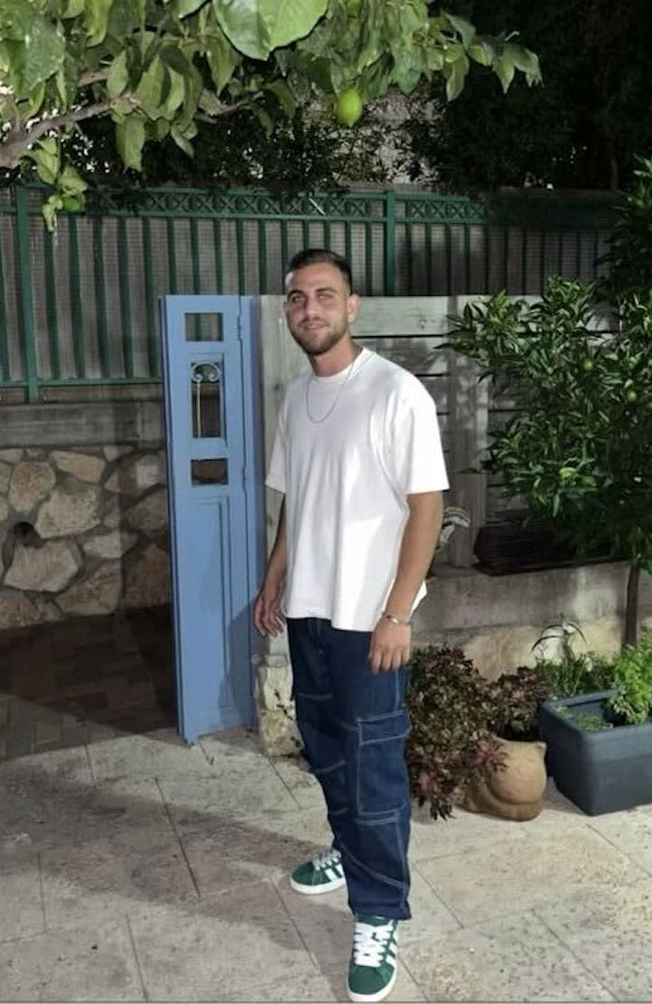 A picture of a smiling Itay Glisko in jeans, t-shirt, and green Adidas sneakers.