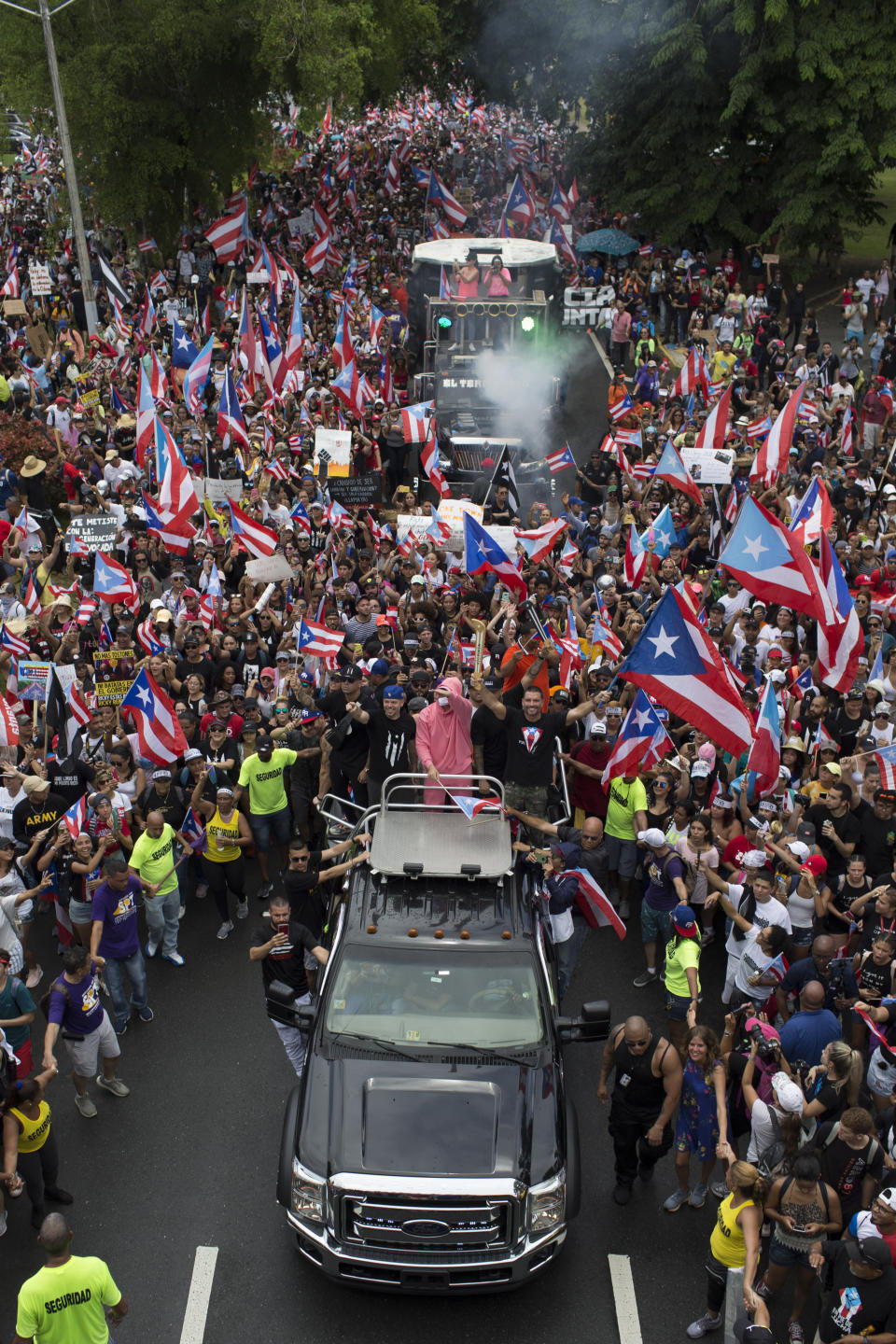 FILE - In this July 25, 2019 file photo, Puerto Rican singer Rene Perez Joglar, also known has Residente, center left in blue cap, and Bad Bunny, center dressed in pink, ride a top a vehicle in a march to celebrate the resignation of Gov. Ricardo Rossello, in San Juan, Puerto Rico. Both celebrities joined the protests that forced Rossello to announce hi resignation from office. (AP Photo/Dennis M. Rivera Pichardo, File)