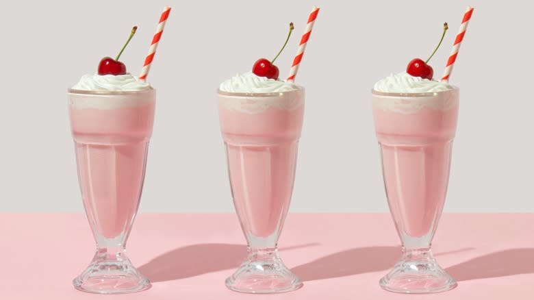 Three pink milkshakes with cherries and straws in a row