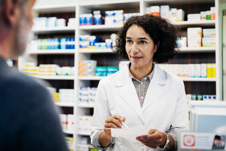 A pharmacist talking while handing a prescription to a customer.