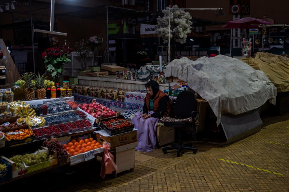 A fruit vendor waits for customers inside a dark market in downtown Kyiv, Ukraine, on Monday. The city is struggling to keep the lights on amid Russian assaults on the electrical grid.