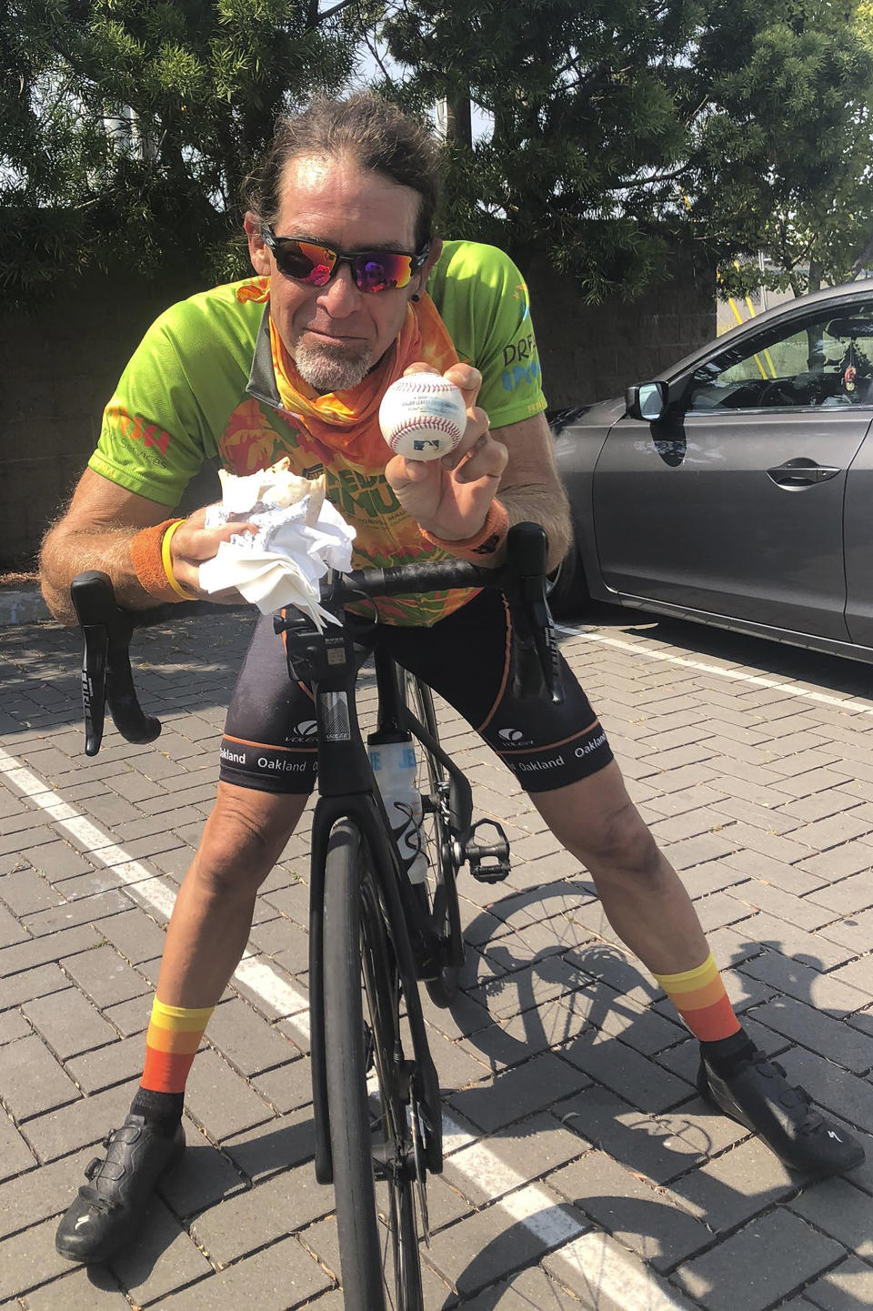 Avid baseball fan and cyclist Mark Pelzner poses with his foul ball, Sunday, Sept. 6, 2020, in Alameda, Calif. (AP Photo/Janie McCauley)