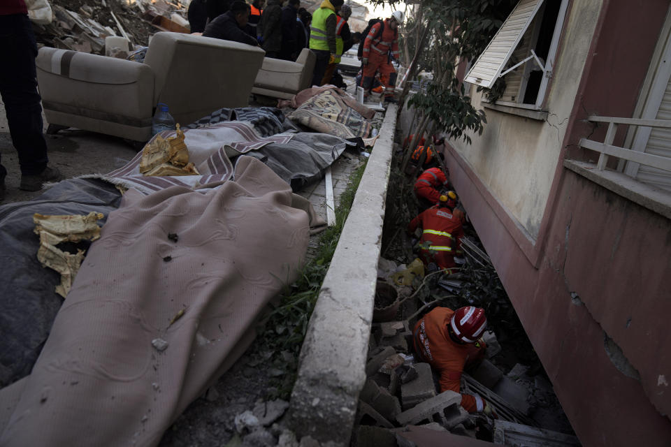 FILE - Dead bodies covered with blankets are seen on the ground next to members of the British rescue team searching in a destroyed building in Antakya, southern Turkey, Feb. 9, 2023. A year after the devastating 7.8 magnitude earthquake struck southern Turkey and northwestern Syria, a massive rebuilding effort is still trudging along. The quake caused widespread destruction and the loss of over 59,000 lives. (AP Photo/Khalil Hamra, File)