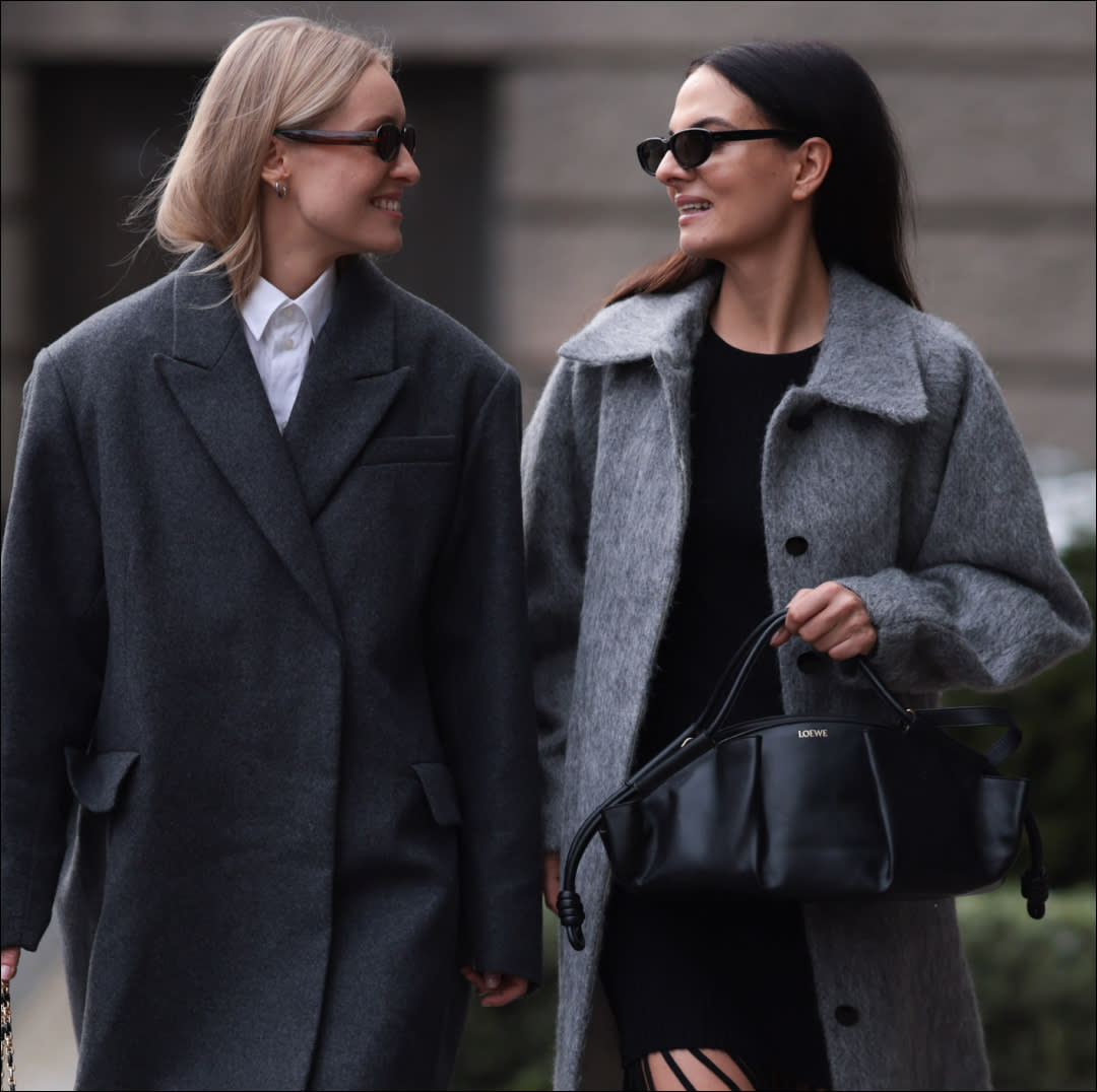  Marlies Pia Pfeifhofer (L) seen wearing brown oval sunglasses, silver earrings, white cotton buttoned blouse / shirt, COS dark grey short oversized wool coat, Dior black / white herringbone checked pattern suit vest / matching blazer jacket and suit pants, Dior black / white tweed crossbody bag, Dior black shiny leather loafers; Anna Winter (R) seen wearing Celine black sunglasses, Ganni black fringed short dress, Ganni light grey wool long coat, Loewe black leather handbag and Prada black shiny leather boots, on November 30, 2023 in Berlin, Germany. (Photo by Jeremy Moeller/Getty Images). 