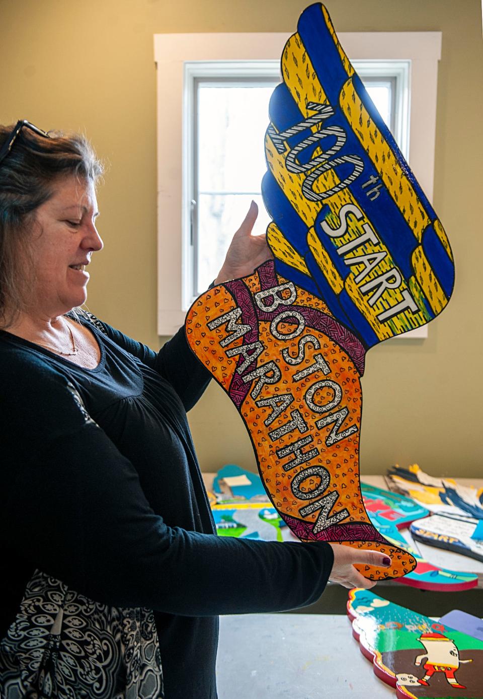 Kelly Grill, executive director for the Hopkinton Center for the Arts, admires one of the 26 "feet" that are part of the Winged Foot Exhibition that will be on display from April 1-21 on the Hopkinton Town Green in recognition of 100 years since the Boston Marathon started in Hopkinton, March 27, 2024. The winged feet will be auctioned off online to benefit the HCA and the 26.2 Foundation. The HCA also offers "The Start Line Experience," a self-guided art and education tour of Marathond Legend sculptures in Hopkinton. Finally, a mural marking the 100 years of Hopkinton starts will be placed at the Hopkinton Public Library.