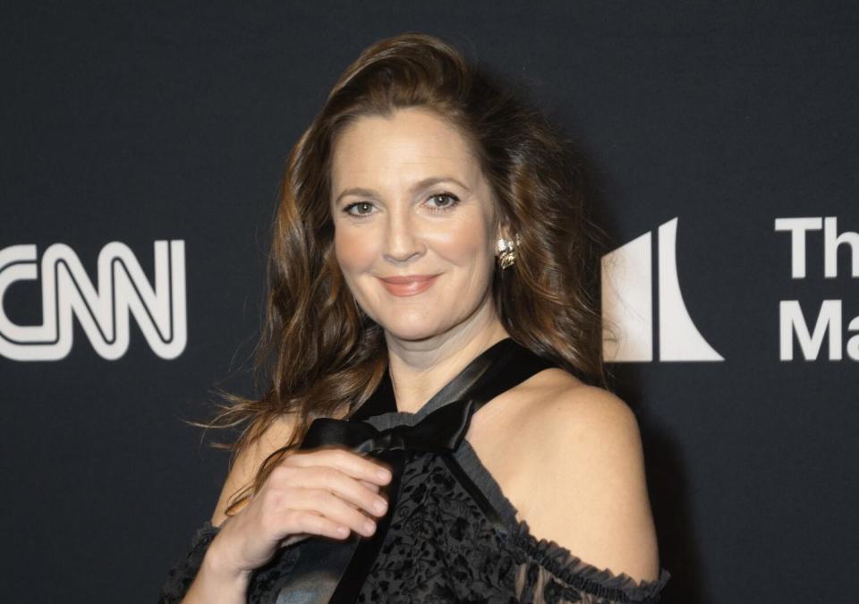 Drew Barrymore poses in a black, lacy dress in front of a black backdrop.