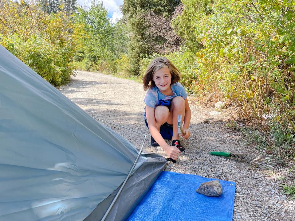 Smiling girl hammering peg for tent into ground