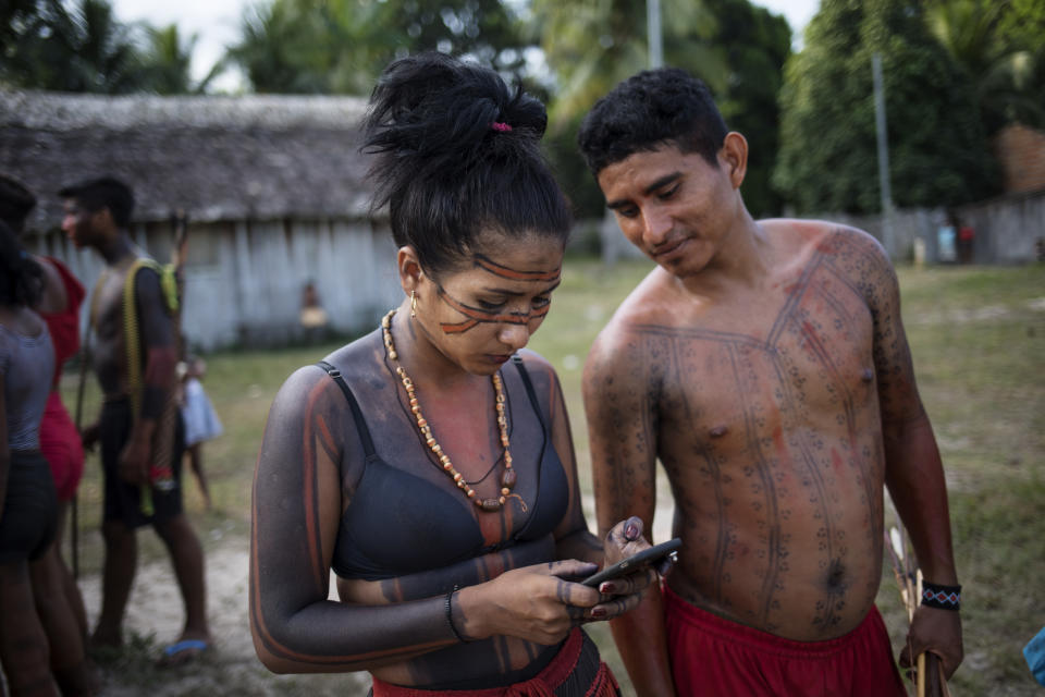 In this Sept. 3, 2019 photo, a woman checks her cell phone during a meeting of Tembé tribes at the Tekohaw indigenous reserve, Para state, Brazil. Some saw hope in the sustainable development plan presented this week at the meeting in the village of Tekohaw. It would include drones and other technology to curb the encroachers. (AP Photo/Rodrigo Abd)