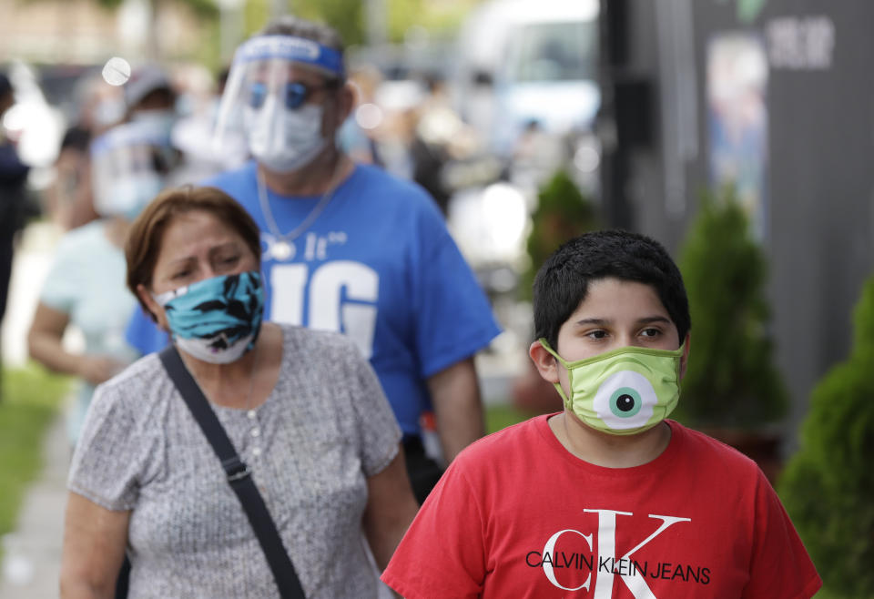 People, social distancing and wearing masks to prevent the spread of the new coronavirus, wait in line at a mask distribution event, Friday, June 26, 2020, in a COVID-19 hotspot of the Little Havana neighborhood of Miami. Florida banned alcohol consumption at its bars Friday as its daily confirmed coronavirus cases neared 9,000, a new record that is almost double the previous mark set just two days ago. (AP Photo/Wilfredo Lee)
