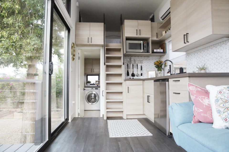 Two-level tiny home interior with kitchen, staircase, and seating area with gray floor