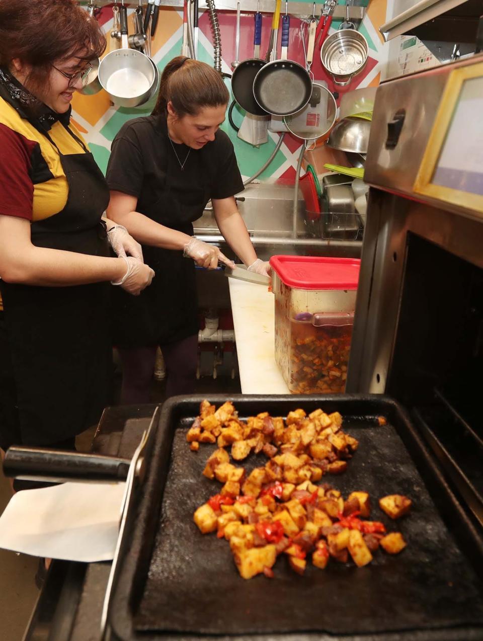 Kass LaVictoire, left, former owner of NOMZ in the Northside Marketplace, instructs new co-owner Jamie Krum on how to prepare a NOMZ dish March 23 in Akron.