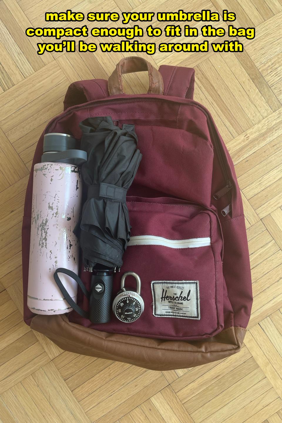 A backpack on the floor with a water bottle, compact umbrella, padlock, and text reading 