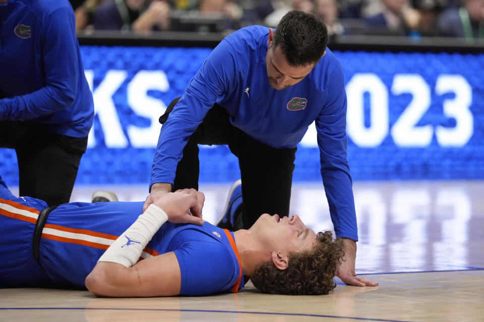 FILE - Florida head coach Todd Golden kneels next to center Micah Handlogten (3) after he injured his leg during the first half of an NCAA college basketball game against Auburn at the Southeastern Conference tournament, Sunday, March 17, 2024, in Nashville, Tenn. Handlogten will take a year off to fully recover from a broken left leg suffered in the Southeastern Conference championship game last month. (AP Photo/John Bazemore, File)