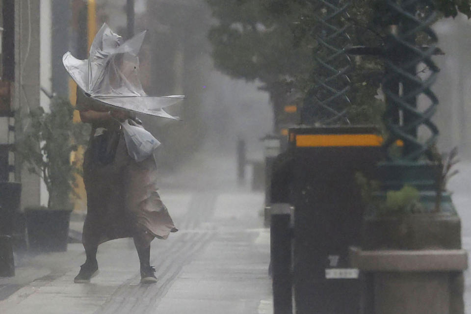 A woman makes her way through the strong wind and rain in Miyazaki, southern Japan, Sunday, Sept. 18, 2022, as a powerful typhoon pounded southern Japan. (Kyodo News via AP)