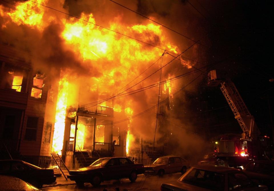 Fire has spread from 98 Oak St. to No. 100, on the right, and No. 96, on the left, on March 14, 2003. The sliver of an alley, behind that propped-up ladder in the lower left, was the only way out for three members of the Velez family.