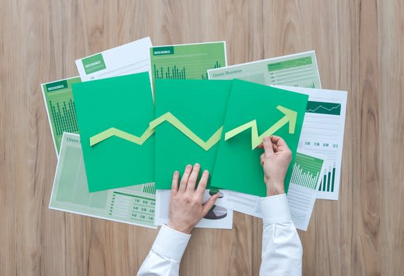 A person arranges cut-up pieces of construction paper into an ascending arrow.