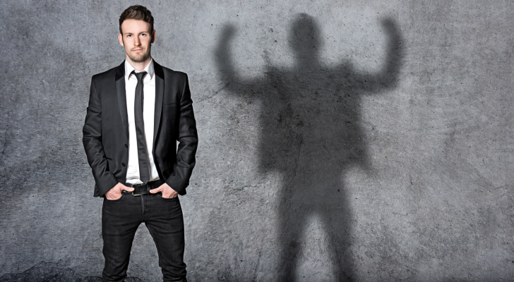 An image of a businessman standing facing the camera with his hands in his pockets, his shadow projected behind him with his arms up and flexing