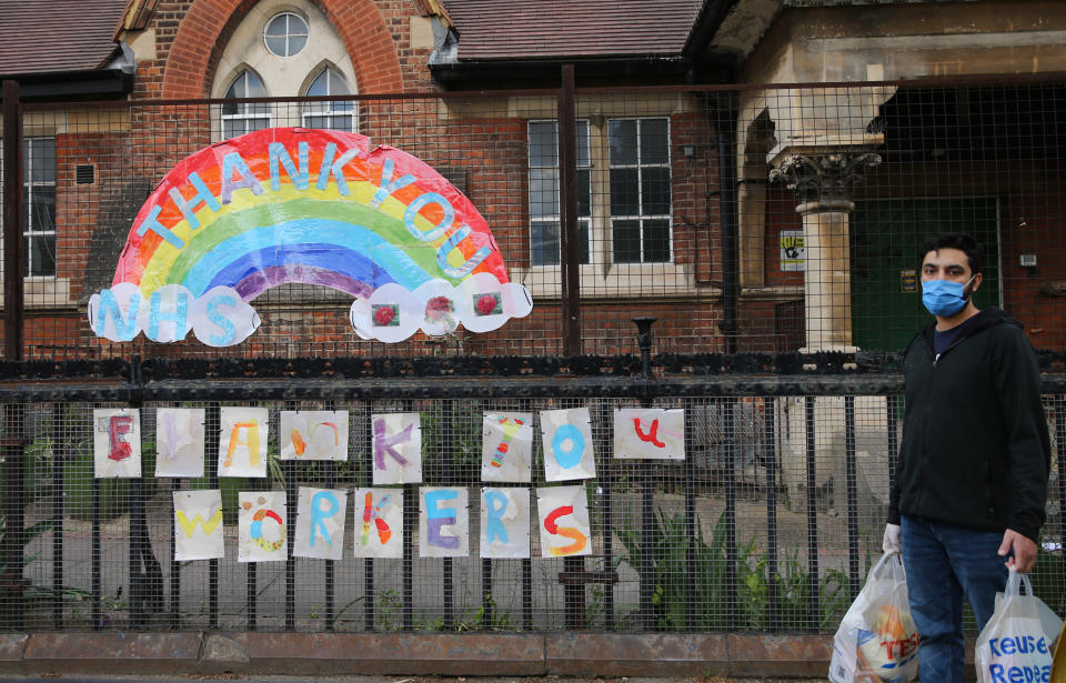 A man wearing a face mask walks past a rainbow with messages thanking key workers, outside Colvestone Primary School in Dalston, Hackney, east London, as the UK continues in lockdown to help curb the spread of the coronavirus. Picture date: Saturday May 2, 2020.