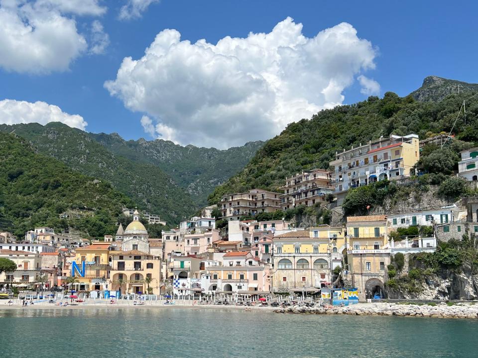 Colorful buildings by the sea with greenery-covered mountains in the background.