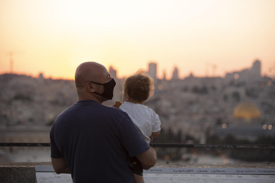 A man wearing a mask to curb the spread of the coronavirus, holds a child on an overlook at the Mount of Olives as they watch the sun set behind the Dome of the Rock Mosque in Jerusalem, Wednesday, Sept. 2, 2020. (AP Photo/Maya Alleruzzo)