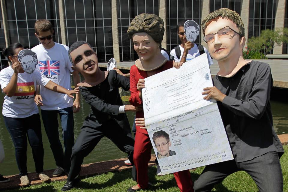 Activistas con máscaras que representan al presidente de EEUU, Barack Obama, izquierda; a la presidenta brasileña Dilma Rousseff, centro, y al exanalista estadounidense de inteligencia Edward Snowden sostienen una pancarta que imita el pasaporte de Snowden en las afueras del ministerio de Relaciones Exteriores en Brasilia, Brasil, el jueves 13 de febrero de 2014. Activistas y actores entregaron en la cancillería una petición con más de un millón de firmas para que Brasil le conceda asilo al exanalista norteamericano. (AP Photo/Eraldo Peres)