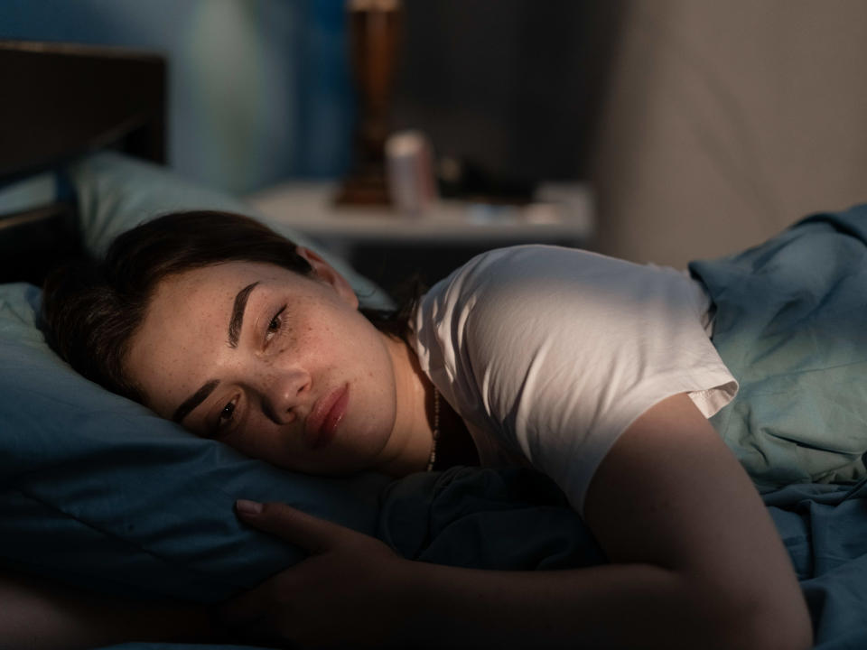 Young sad woman lying in bed late at night trying to sleep suffering insomnia. Girl in bed scared on nightmares looking worried and stressed. Sleeping disorder and insomnia concept