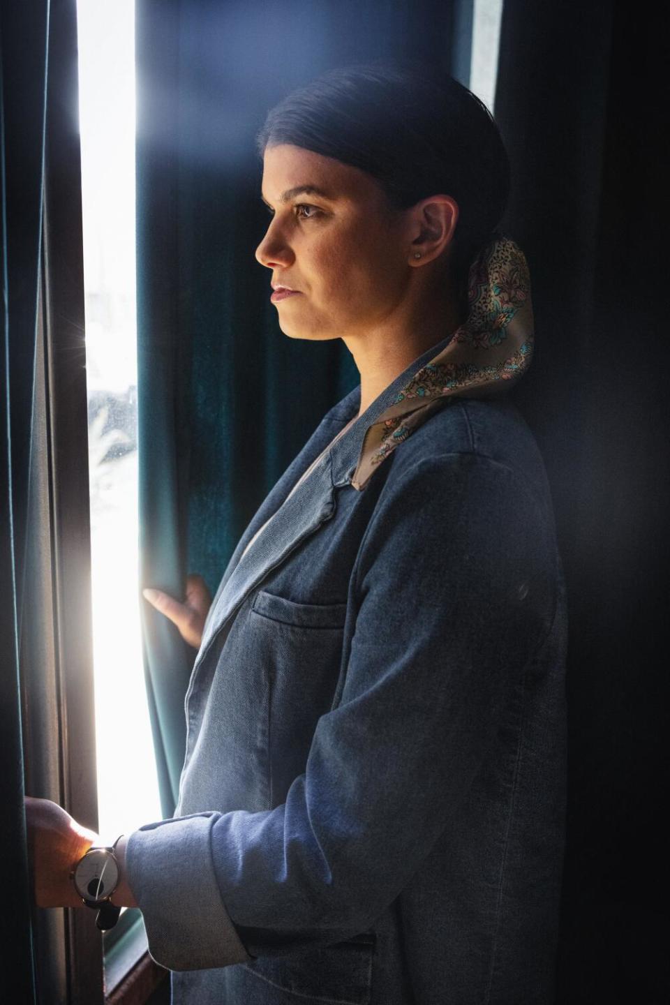 A woman stands, looking out a window.