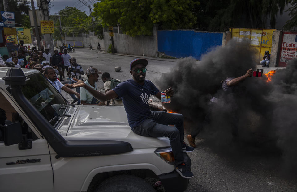 A journalist sits on the hood of a police car as protesters attempt to confiscate the police vehicle during a protest against the death of journalist Romelo Vilsaint, in Port-au-Prince, Haiti, Sunday, Oct. 30, 2022. Vilsaint died Sunday after being shot in the head when police opened fire on reporters demanding the release of one of their colleagues who was detained while covering a protest, witnesses told The Associated Press. (AP Photo/Ramon Espinosa)