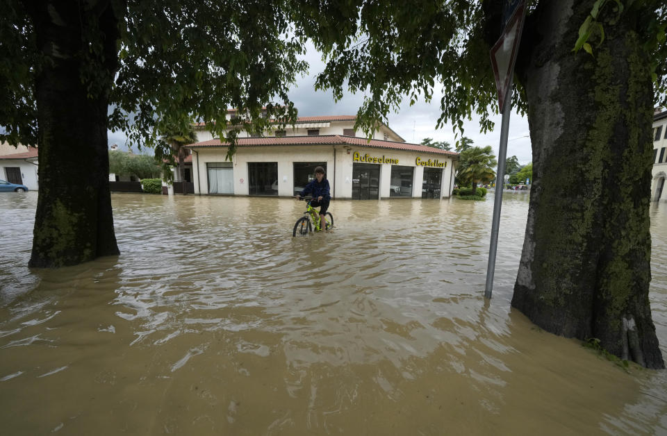 A boy pedals in a flooded street in the village of Castel Bolognese, Italy, Wednesday, May 17, 2023. Exceptional rains Wednesday in a drought-struck region of northern Italy swelled rivers over their banks, killing at least eight people, forcing the evacuation of thousands and prompting officials to warn that Italy needs a national plan to combat climate change-induced flooding. (AP Photo/Luca Bruno)