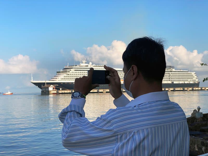 Man uses a phone to take a picture in front of the cruise ship MS Westerdam at dock in the Cambodian port of Sihanoukville