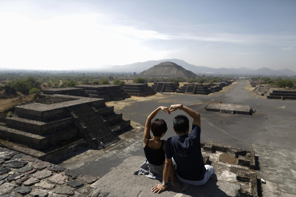 South Korean tourists Myung Hee Lee, left, and Byung Ho Im, form a heart with their hands as they pose for pictures atop the Pyramid of the Moon, in Teotihuacan, Mexico, Thursday, March 19, 2020. The pair took advantage of getting stuck in Mexico City for a day to visit the pyramids, after their flight home from a vacation in Cancun and Cuba was cancelled. To slow the spread of the new coronavirus, authorities announced Wednesday that they would close the pyramid complex on weekends, beginning Saturday, March 21, when thousands of visitors typically climb the Pyramid of the Sun to celebrate the Spring equinox.(AP Photo/Rebecca Blackwell)