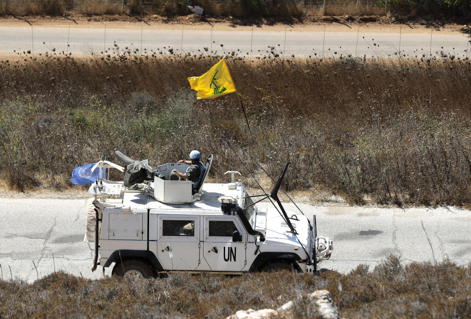 Spanish UN peacekeepers patrolling along the Lebanese-Israeli border pass a Hezbollah flag, in the southern Lebanese village of Kfar Kila, Lebanon, Monday, Sept. 2, 2019. The Lebanon-Israel border was mostly calm with U.N. peacekeepers patrolling the border Monday, a day after the Lebanese militant Hezbollah group fired a barrage of anti-tank missiles into Israel, triggering Israeli artillery fire that lasted less than two hours and caused some fires. (AP Photo/Hussein Malla)