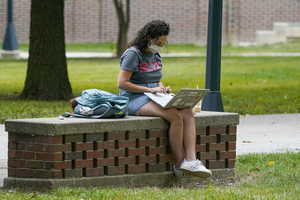 A masked student works on her laptop on the campus of Ball State University in Muncie, Ind., Thursday, Sept. 10, 2020. College towns across the U.S. have emerged as coronavirus hot spots in recent weeks as schools struggle to contain the virus. Out of nearly 600 students tested for the virus at Ball State, more than half have returned been found positive, according to data reported by the school. Dozens of infections have been blamed on off-campus parties, prompting university officials to admonish students. (AP Photo/Michael Conroy)