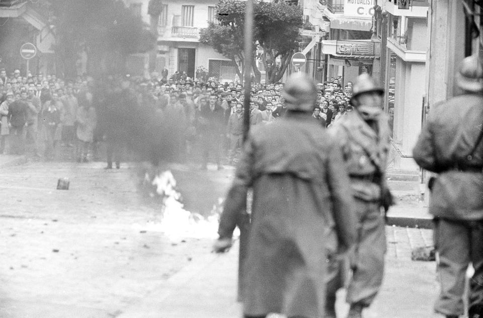 FILE - In this Dec.10, 1960 file photo, Algerian demonstrators watch as gasoline filled bottle burns in a street of Algiers, protesting the arrival of French President Charles De Gaulle in Algeria to promote his self-determination policy. French President Emmanuel Macron announced a decision to speed up the declassification of secret documents related to Algeria's seven-year war of independence from 1954 to 1962. (AP Photo, File)