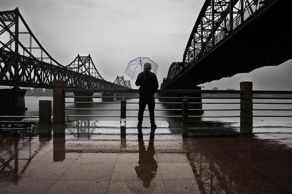 <p>A Chinese man stands in the rain between “Friendship Bridge”, left, and “Broken Bridge”, right, as he looks across the Yalu river from the border city of Dandong, Liaoning province, northern China towards the city of Sinuiju, North Korea on May 23, 2017 in Dandong, China. (Photo: Kevin Frayer/Getty Images) </p>