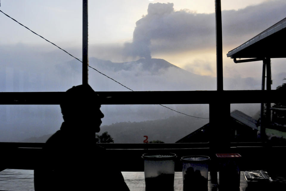 A man sits in coffee shop as Mount Marapi spews volcanic ash from its crater, in Agam, West Sumatra, Indonesia, Tuesday, Dec. 5, 2023. Indonesian authorities halted Monday the search for a dozen of climbers after Mount Marapi volcano erupted again, unleashing a new burst of hot ash as high as 800 meters (2,620 feet) into the air, officials said. (AP Photo/Ardhy Fernando)