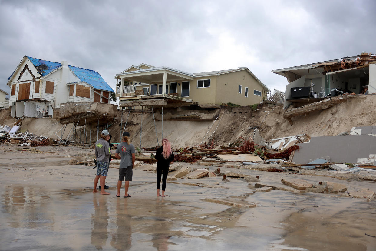 Four people on the beach stare at three homes on a cliff face that has been washed away by the storm. 