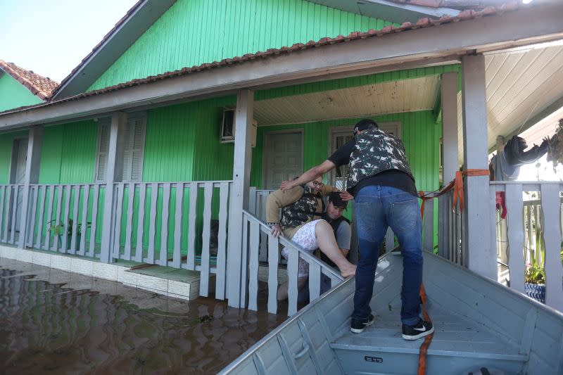 People assist a woman as she leaves her flooded house, in Venancio Aires