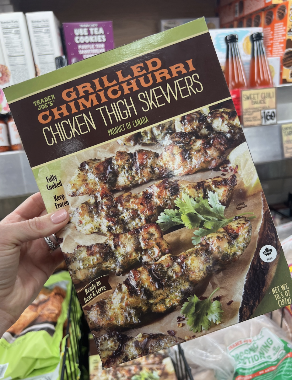 A hand holds a package of Trader Joe's Grilled Chimichurri Chicken Thigh Skewers.