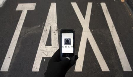 Photo illustration of logo of car-sharing service app Uber on a smartphone over a reserved lane for taxis in a street in Madrid