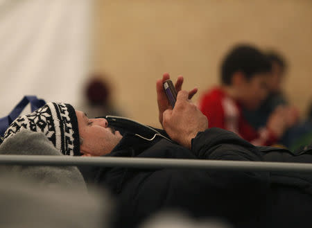 A man uses a mobile device as migrants and refugees wait to continue their train journey to western Europe at a refugee transit camp in Sid, Serbia, February 11, 2016.REUTERS/Darrin Zammit Lupi