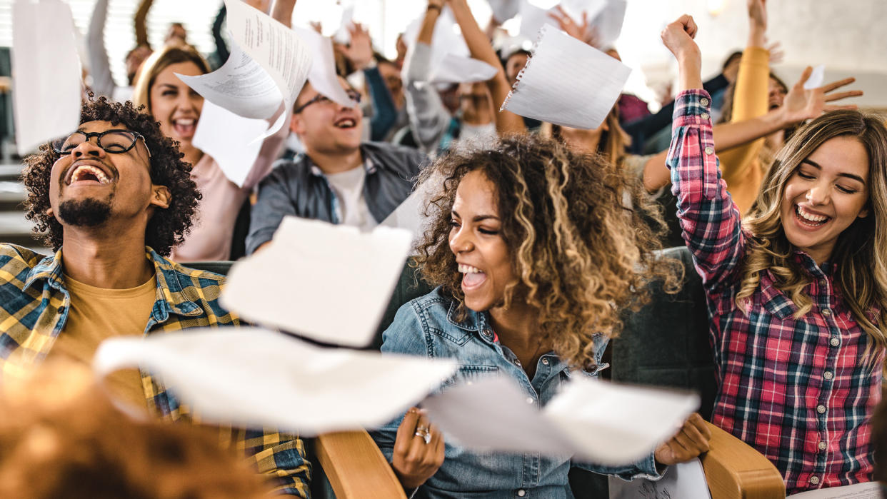 Large group of cheerful college students having fun while throwing papers in a lecture hall.