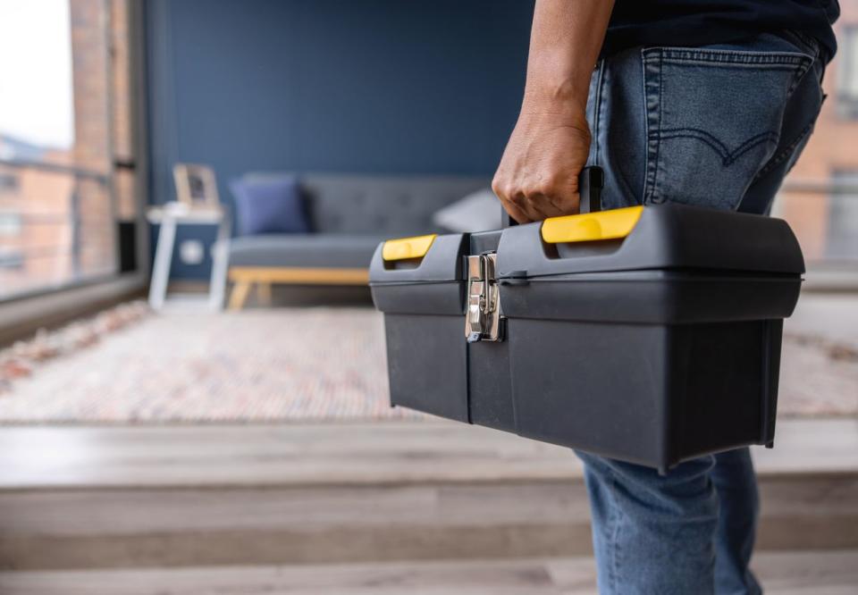 A person is seen carrying a black and yellow tool box into a living room.